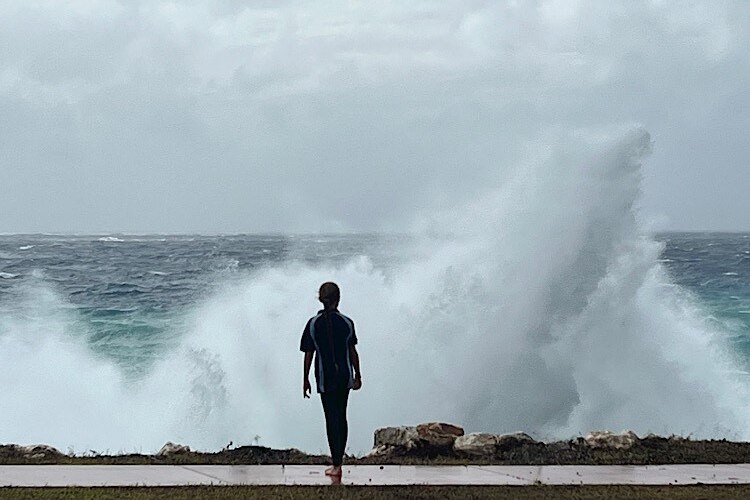 A child watches on as waves crash into rocks on the foreshore at Christmas Island, sending water spray into the air.