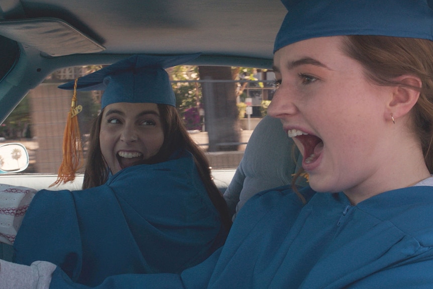 Colour film still of Beanie Feldstein and Kaitlyn Dever driving and yelling in 2019 film Booksmart.