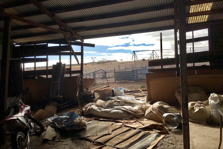 A shearing shed with a wall blown off.