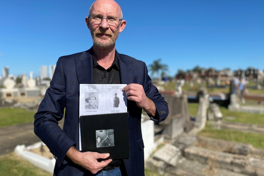 A man holds black and white pictures at a cemetery.