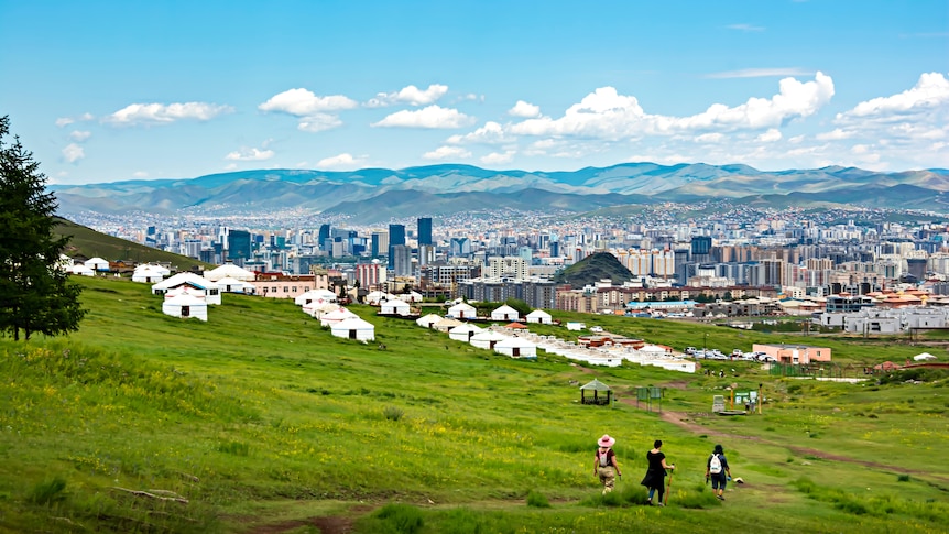 a vast view with mountains in the distance and city scape with tradition yurt homes in the foreground where 3 people are hikingr