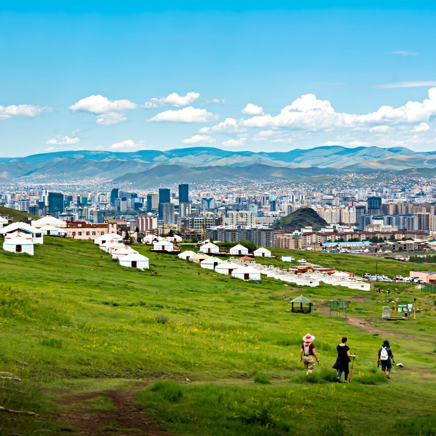 a vast view with mountains in the distance and city scape with tradition yurt homes in the foreground where 3 people are hikingr