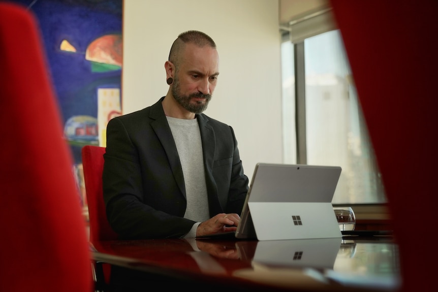 a man sits at a desk typing on a small laptop