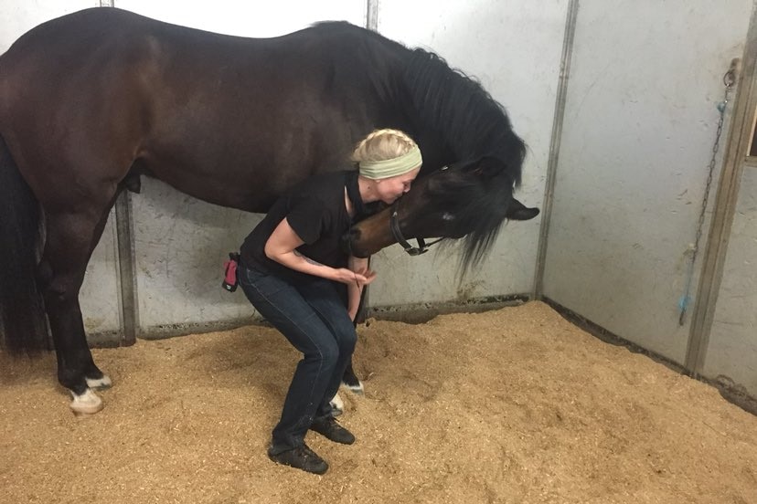 A young woman bends down to nuzzle the head of a horse affectionately.