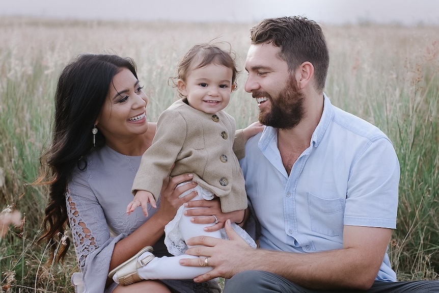 A close up of Melissa, daughter Violet and husband Doug Cannon sitting in a field of grass.