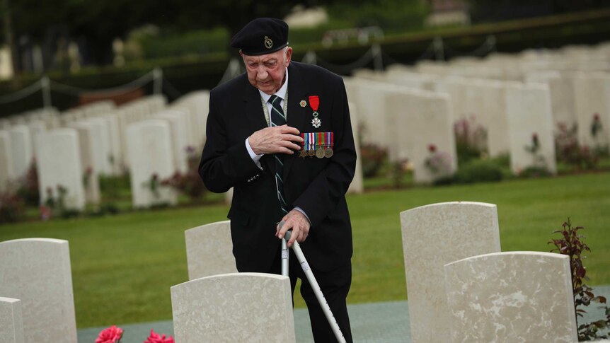 A World War II veteran crosses himself in front of British soldier burial fallen during the WWII.