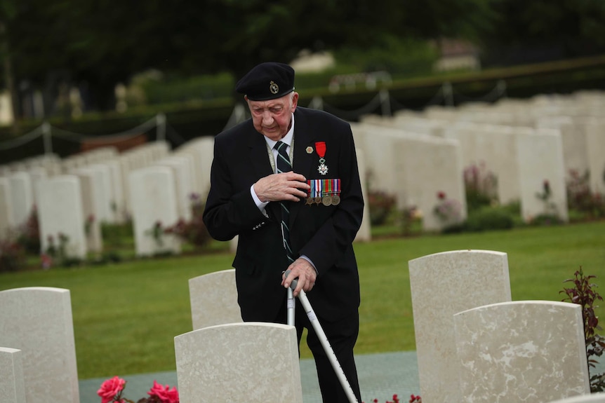 A World War II veteran crosses himself in front of British soldier burial fallen during the WWII.