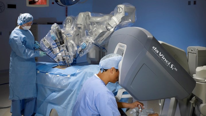 Surgeon in foreground looking into booth with surgeon in background both in blue scrubs .