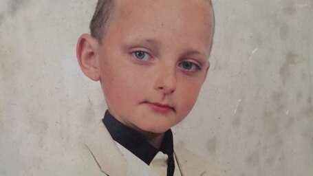 A young Jacob Cummins poses for a photo wearing a white tuxedo.