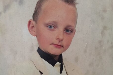 A young Jacob Cummins poses for a photo wearing a white tuxedo.