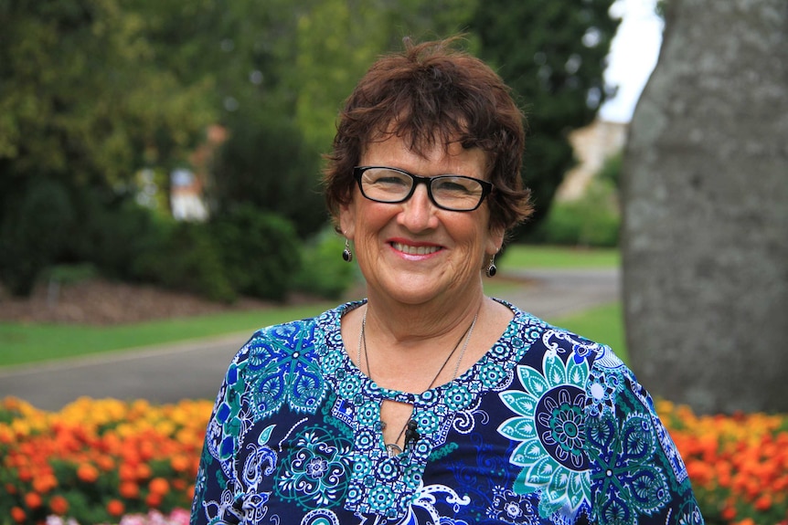 A woman wearing glasses stands in a park.