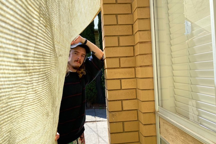 A man in a grey shirt peeks through a sheet.