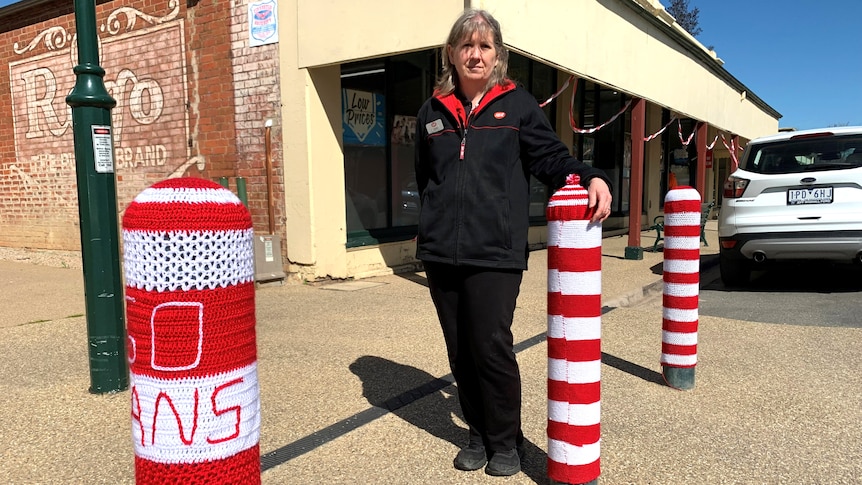Jodie Sorensen leans on a red and white crochet covered bollard on the side of a street.