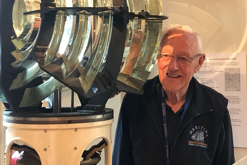 Photograph of a old man standing next to, and lit by a lighthouse light.