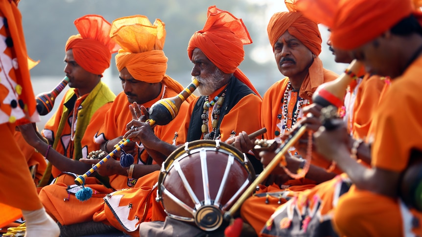 Seated men in orange costumes playing wind and percussion instruments. 