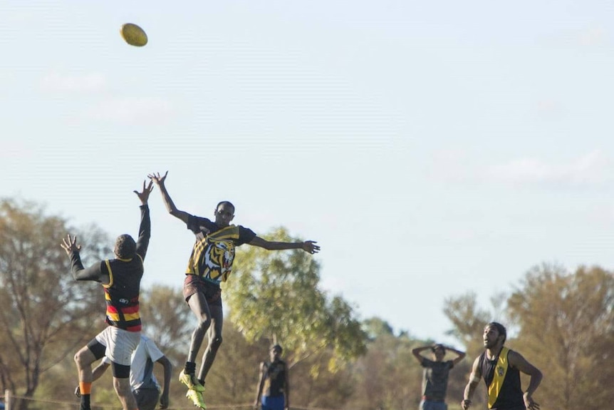 Players leap to get the ball at an amateur AFL match played on grass.