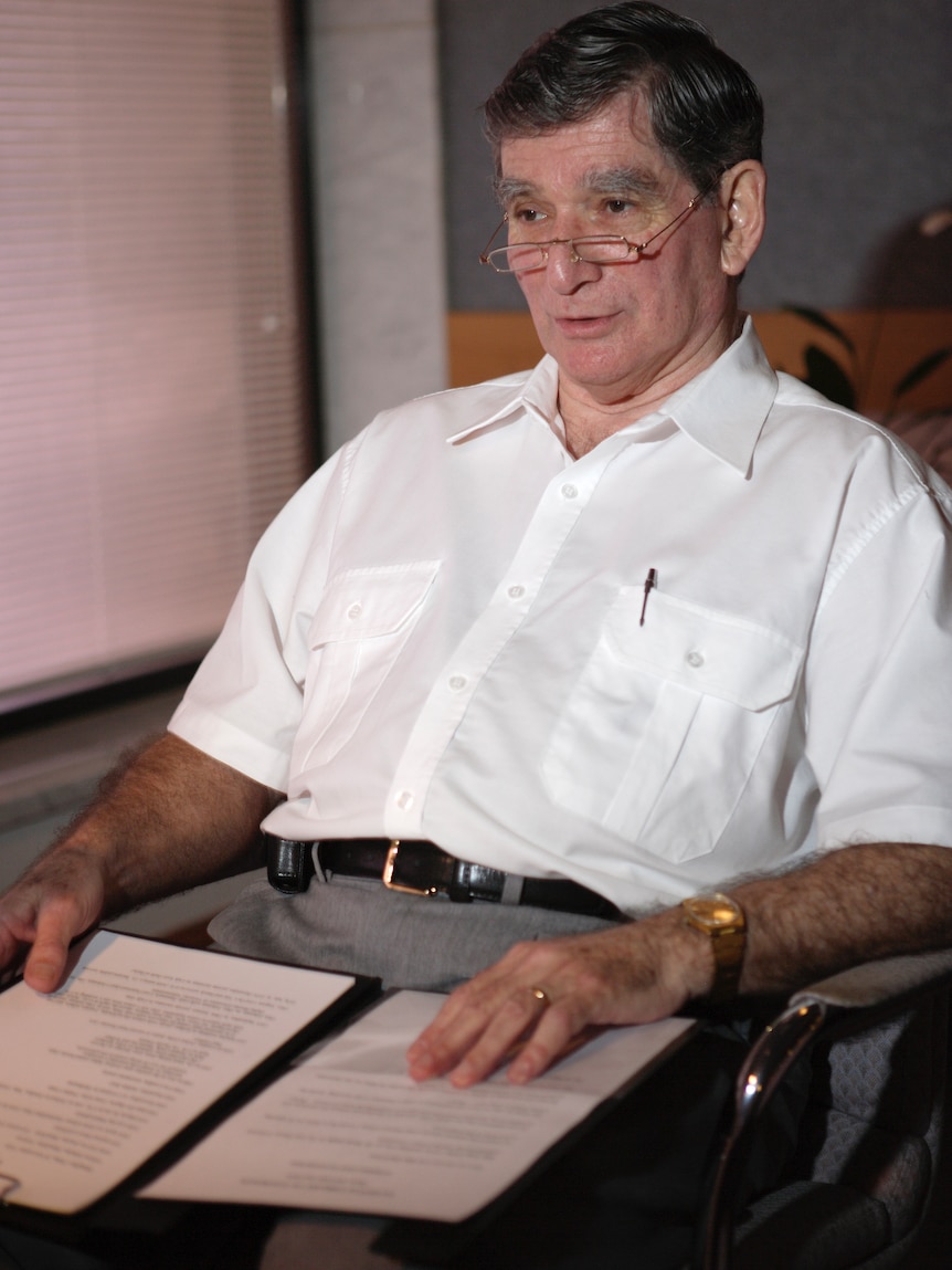 A man in a white shirt and glasses sitting in a chair.