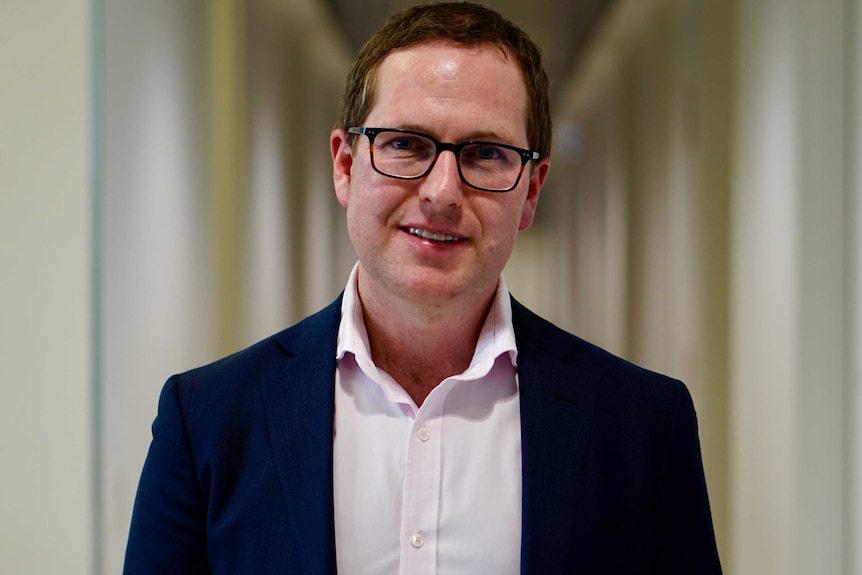 Linear CEO Jayden Rogers stands in a corridor in the screening facility in Perth wearing a suit and glasses.