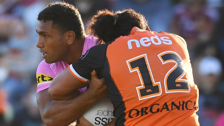 A Penrith Panthers NRL player holds the ball while being tackled by a Wests Tigers opponent.