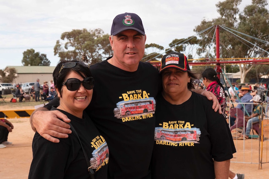 A man and two women pose for the camera with their arms around each other.