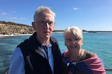 Ian and Claire White smile at the camera. They are outside and in front of a beautiful, blue ocean.