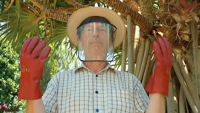 Man standing with gloved arms held up and wearing a face safety shield