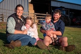 family of five including mother, father two toddlers and a baby sitting on grass in front of farm shed