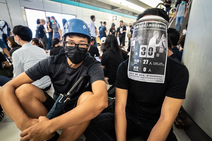 Hong Kong protestors sit while wearing items that hide their faces from being recognized.