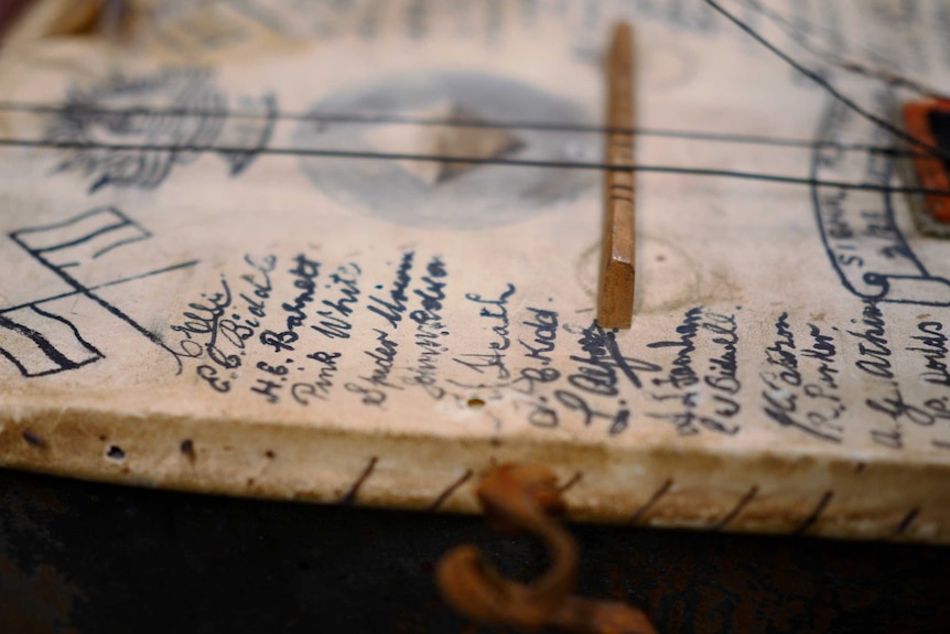 A close up of a handmade banjo with the names of Australian soldiers in the Siege of Tobruk handwritten on the front of it.