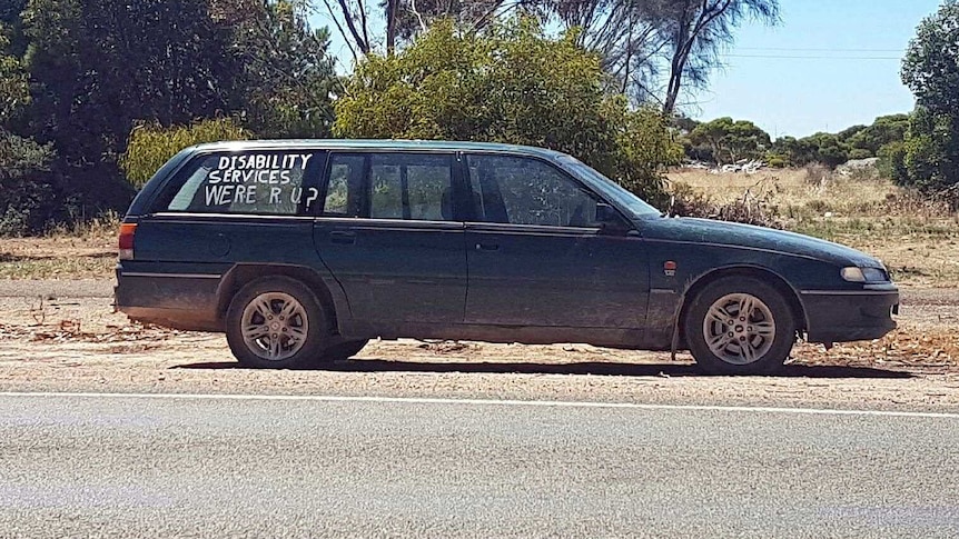 A car at the side of road has words about disability services.