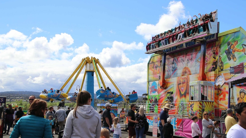 Spectators walk past carnival rides at an agricultural show