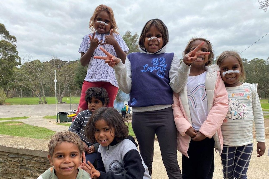 A group of Aboriginal children with white paint on their noses in front of a lawn