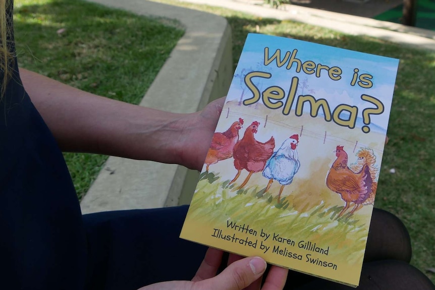 Woman's hands holding a book, entitled, Where is Selma and pictures three hens and a rooster