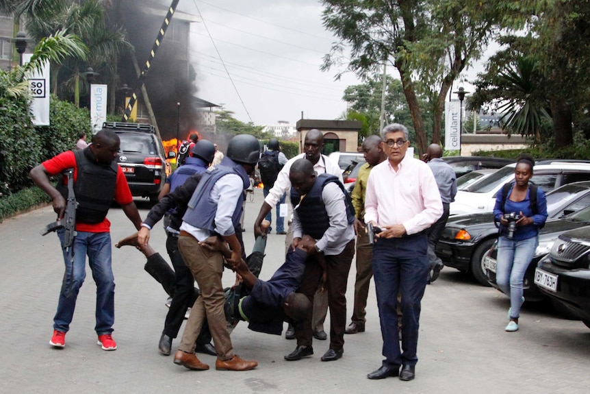 Security forces carry a man face down as smoke rises in the background.