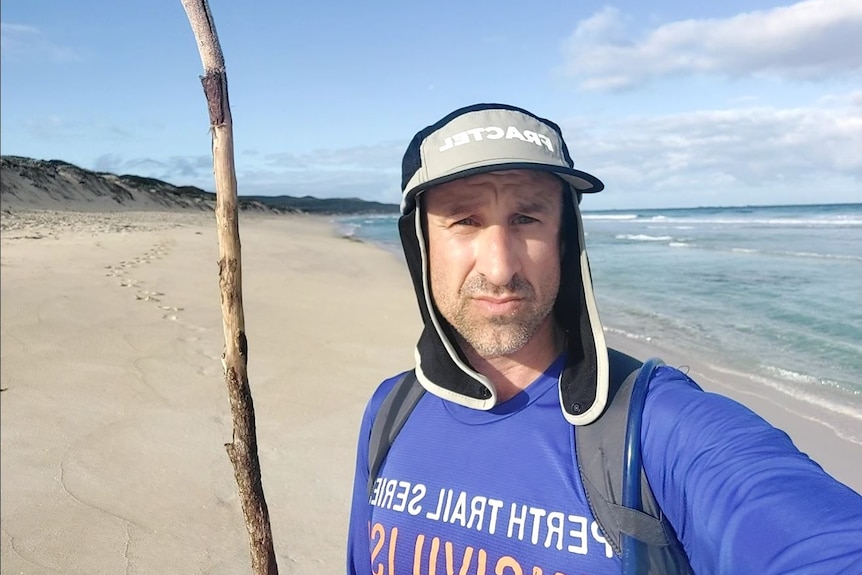 A close of man holding a stick with a white sandy beach in the background