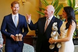 older man standing between smiling couple who are holding small shoes and kangaroo soft toy