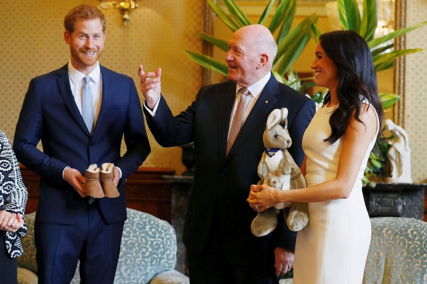 older man standing between smiling couple who are holding small shoes and kangaroo soft toy