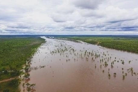 A wide, brown, river flows into the far distance, in the foreground, you can see a four wheel drive parked at the riverside.