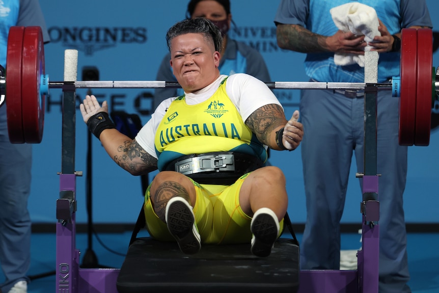 A woman wearing yellow and white celebrates after lifting a weight