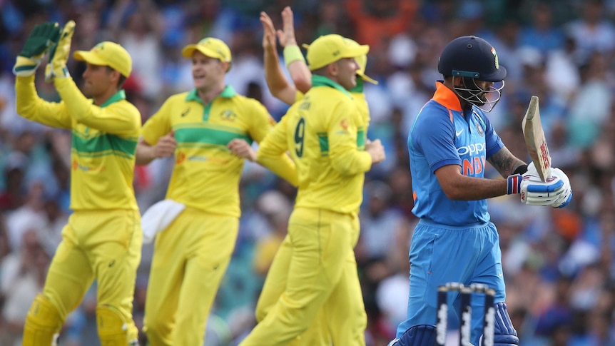 Indian captain Virat Kohli walks off the SCG as Australian cricketers celebrate.