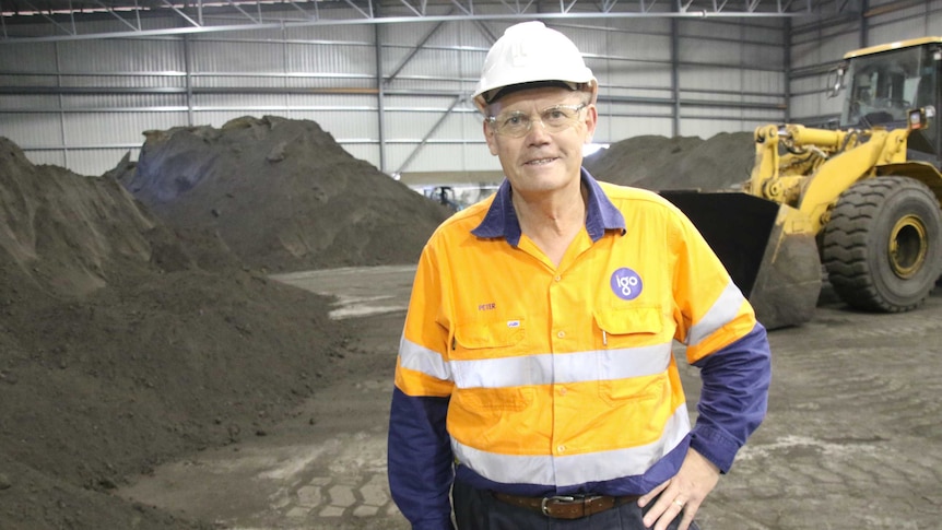 Man in hi-vis work clothes and hard hat standing in a shed with piles of mineral in background.