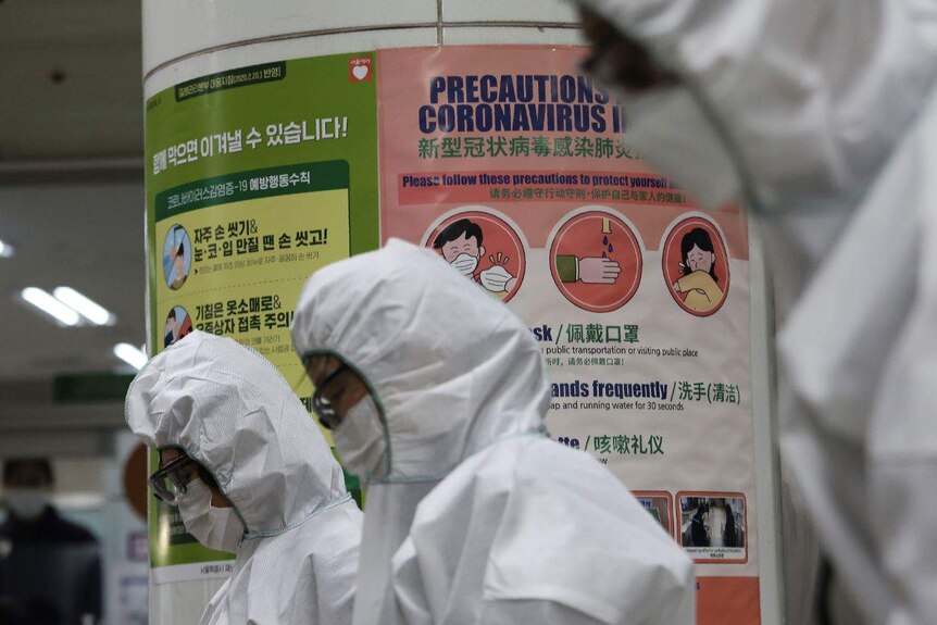 People in white protective suits walk past posters with the words "coronavirus" on them.