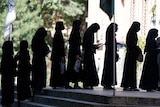 Afghan female students stand in a queue dressed in black abiyas and hijabs.