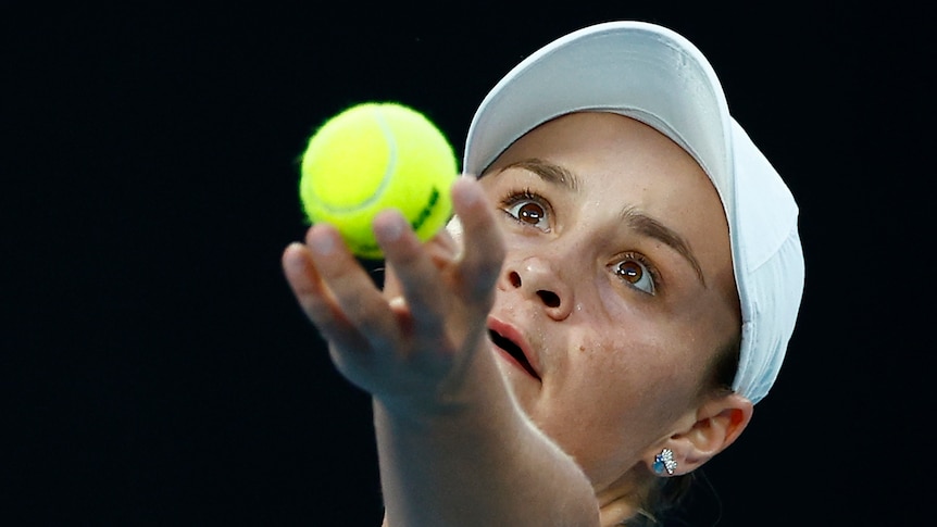An Australian female tennis player holds the ball in the air as she prepares to serve.