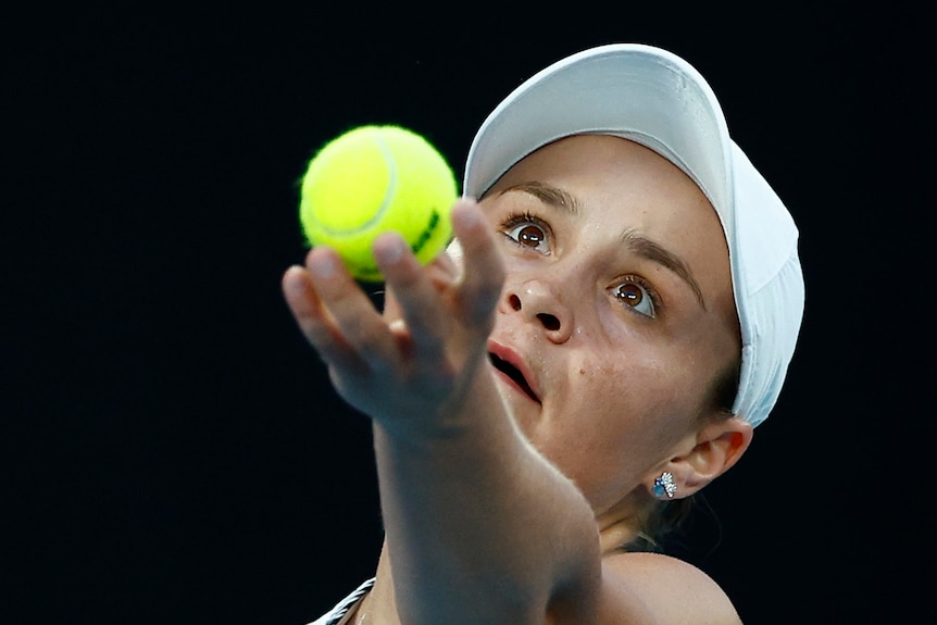 An Australian female tennis player holds the ball in the air as she prepares to serve.