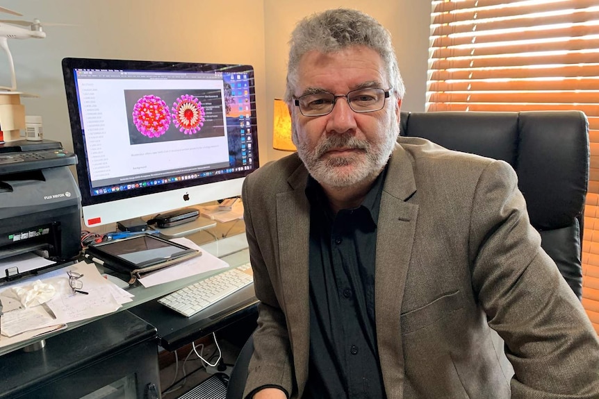 A man sitting in an office with a computer showing an illustration of the COVID-19 virus