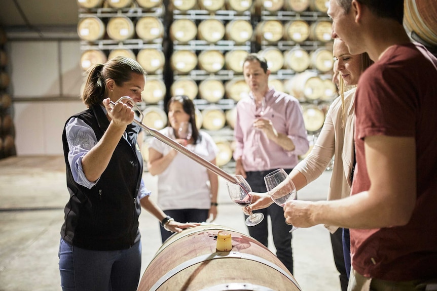 A group of people around barrels taste testing wine