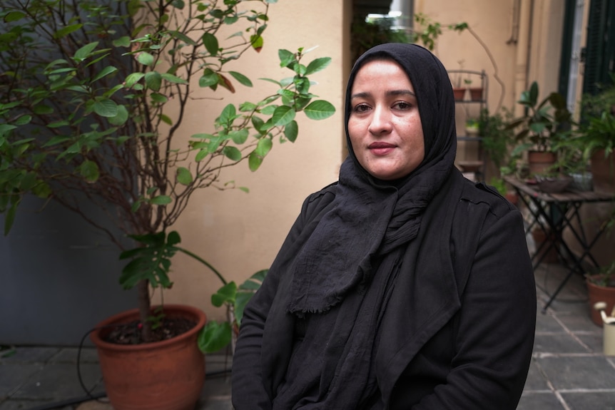 A woman wearing a hijab and black jumper sits on a plane next to two children.