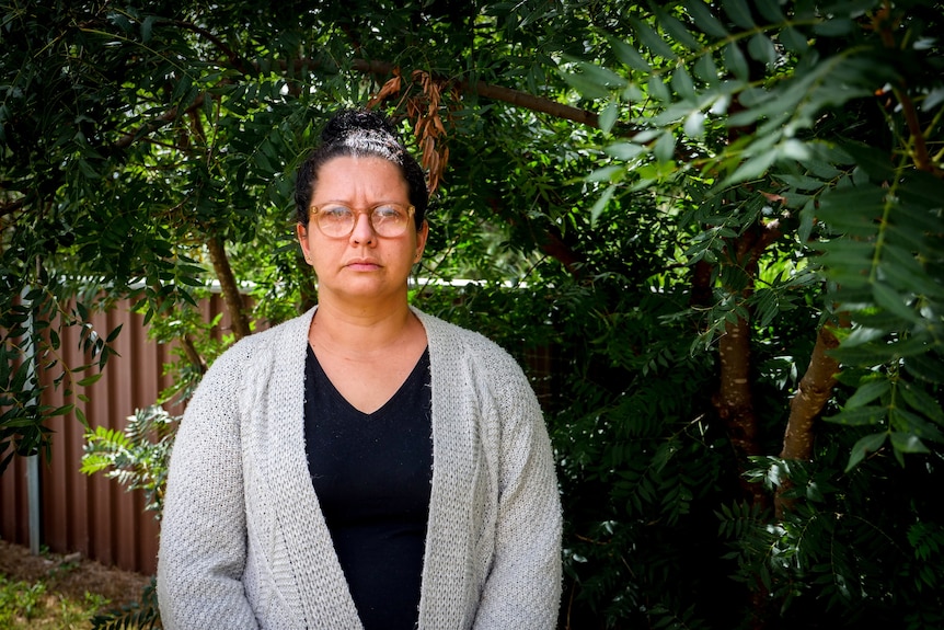 A woman in a grey cardigan stands in front of a tree.