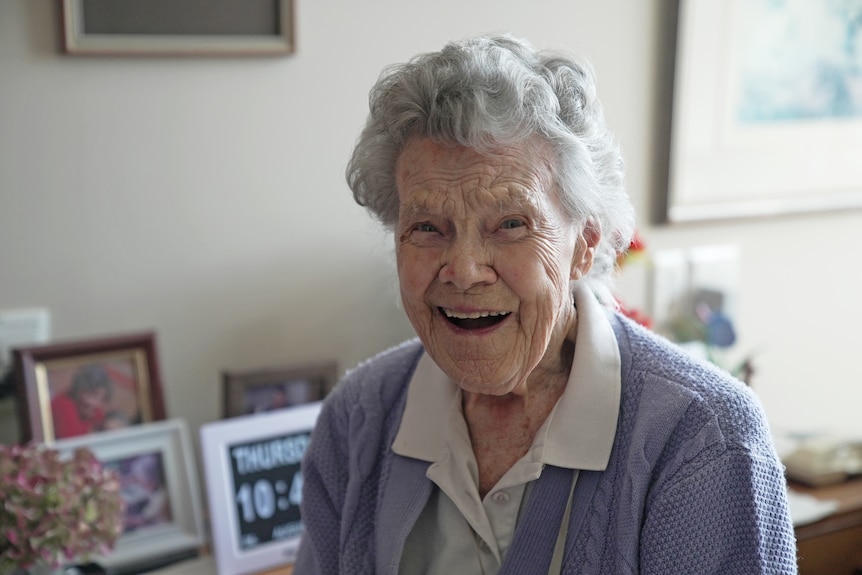 An elderly woman with white hair smiles joyfully.